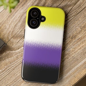 Könnte beinhalten: Eine Smartphone-Hülle mit dem Non-Binary-Pride-Flaggen-Design. Die Hülle hat einen Farbverlauf aus Gelb, Weiß, Lila und Schwarz. Die Handyhülle liegt auf einer Holzoberfläche.