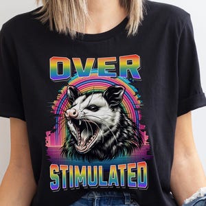 May include: A black t-shirt with a rainbow graphic of an opossum with the text "OVER STIMULATED" in rainbow letters.