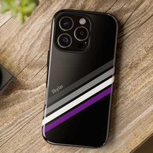 May include: Black phone case with a purple, white and grey stripe design. The case has a raised camera bump and the word "Skylar" printed on the back.