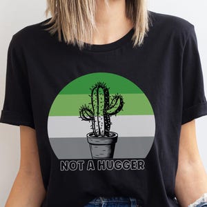 May include: Black t-shirt with a green, gray, and white circle design featuring a cactus in a pot and the text "NOT A HUGGER".