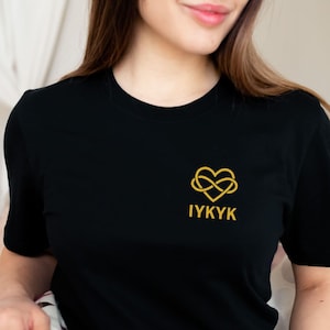 May include: Black t-shirt with a gold infinity heart symbol and the text "IYKYK" on the front.