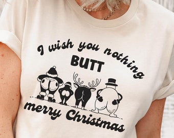 May include: A white t-shirt with a humorous Christmas graphic that reads "I wish you nothing BUTT merry Christmas". The design features a snowman, reindeer, and Santa Claus with their backs to the viewer.
