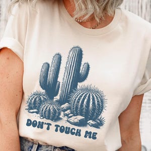 May include: A white t-shirt with a blue cactus graphic and the text "Don't Touch Me".