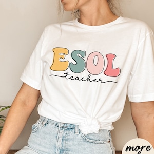 Könnte beinhalten: Weißes T-Shirt mit dem Text "ESOL teacher" in bunten, Retro-Lettern. Die Buchstaben sind schwarz umrandet und mit Gelb, Grün, Rosa und Rot gefüllt.