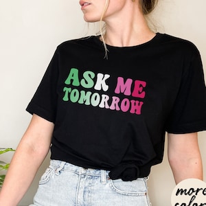 May include: Black t-shirt with the text "ASK ME TOMORROW" in green, pink, and white retro font.