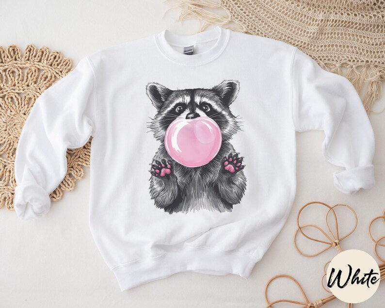 May include: White sweatshirt with a black and white illustration of a raccoon blowing a pink bubble.
