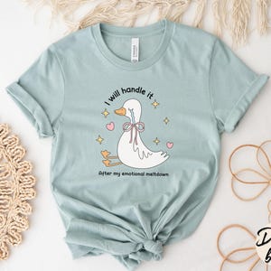 Puede incluir: Una camiseta azul claro con una ilustraci&oacute;n de un pato llorando. El texto en la camiseta dice "Lo manejar&eacute;. Despu&eacute;s de mi colapso emocional."