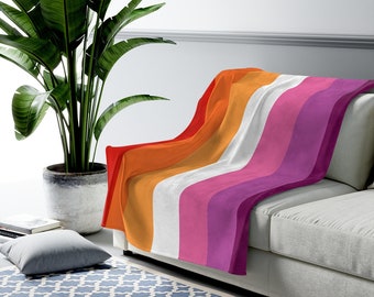 Op de afbeelding: Een zachte, pluche deken met een ontwerp van de lesbische pride-vlag. De deken heeft strepen in oranje, geel, wit, roze en paars.
