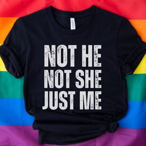 May include: Black t-shirt with white text that reads "Not He Not She Just Me" on a rainbow background.