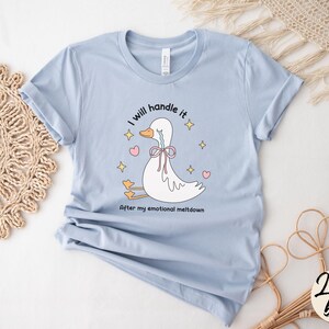 Puede incluir: Camiseta azul claro con una ilustraci&oacute;n de dibujos animados de un pato llorando. El texto de la camiseta dice "Lo manejar&eacute; despu&eacute;s de mi crisis emocional."