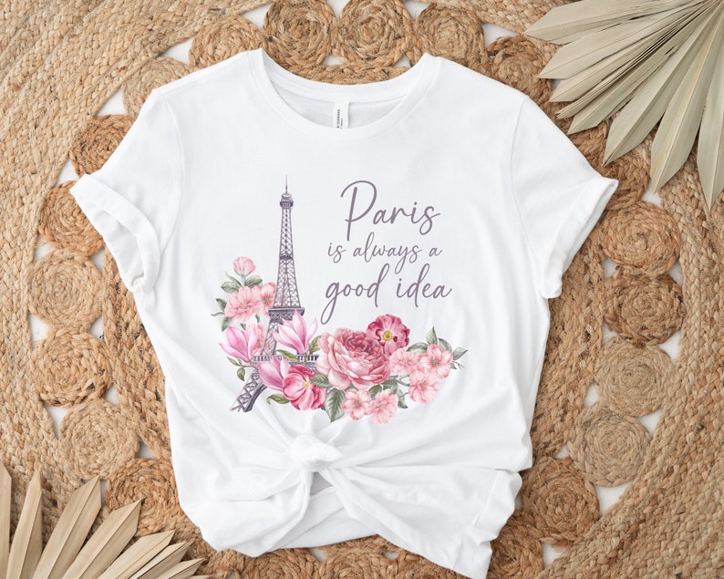 May include: White t-shirt with a design featuring the Eiffel Tower and pink and purple flowers. The text "Paris is always a good idea" is written in a script font. The shirt is knotted at the waist.
