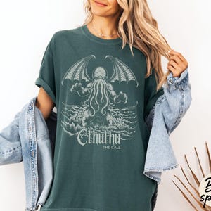 May include: A teal green t-shirt with a graphic print of Cthulhu, a fictional tentacled monster from the works of H.P. Lovecraft. The text "Cthulhu The Call" is printed below the graphic.