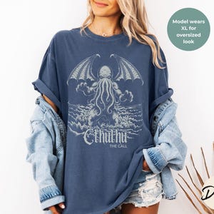 May include: A navy blue t-shirt with a graphic of Cthulhu, a fictional tentacled monster from the works of H.P. Lovecraft. The text "Cthulhu The Call" is printed below the graphic.