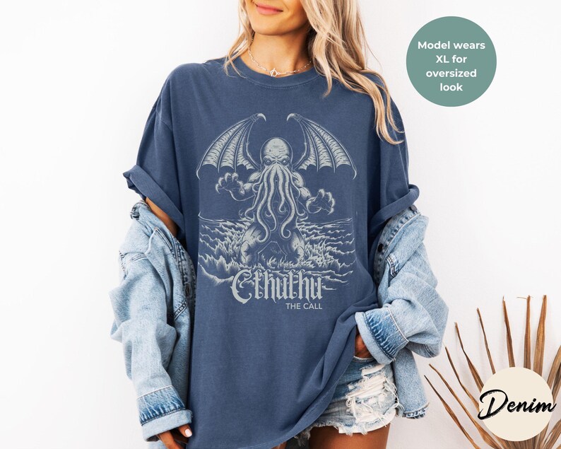 May include: A navy blue t-shirt with a graphic of Cthulhu, a fictional tentacled monster from the works of H.P. Lovecraft. The text "Cthulhu The Call" is printed below the graphic.