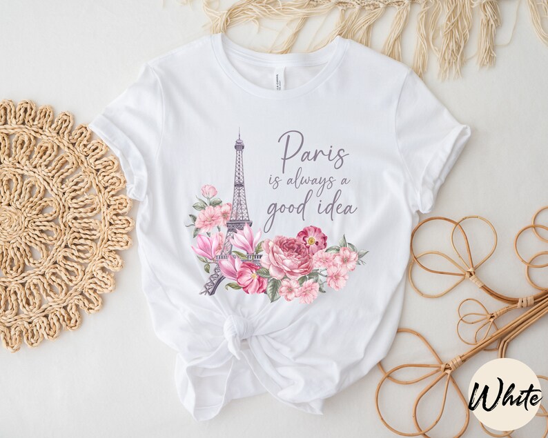 May include: White t-shirt with a design featuring the Eiffel Tower and pink and purple flowers. The text "Paris is always a good idea" is printed above the design. The shirt is tied at the waist.