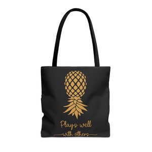 May include: Black tote bag with a gold pineapple graphic and the text "Plays well with others".