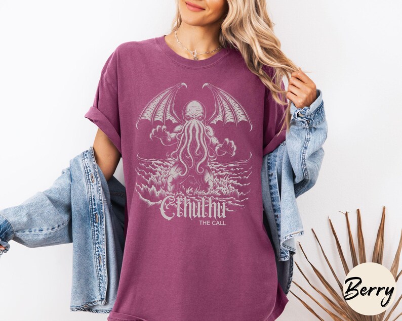 May include: A maroon t-shirt with a white graphic of Cthulhu, a fictional tentacled monster from the works of H.P. Lovecraft. The graphic includes the text "Cthulhu" and "The Call".