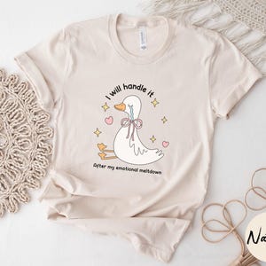 Puede incluir: Una camiseta beige con una ilustraci&oacute;n de dibujos animados de un pato llorando con el texto "Lo manejar&eacute; despu&eacute;s de mi crisis emocional".