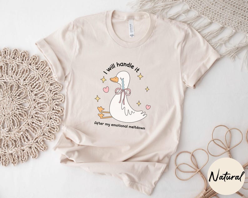 Puede incluir: Una camiseta beige con una ilustraci&oacute;n de dibujos animados de un pato llorando con el texto "Lo manejar&eacute; despu&eacute;s de mi crisis emocional".