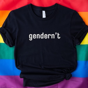 Peut inclure: Un t-shirt noir avec le texte "gendern't" en lettres blanches. Le t-shirt est posé sur un drapeau arc-en-ciel.