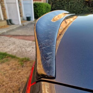 Peut inclure: Gros plan d'un aileron de voiture bleu foncé avec un motif en fibre de carbone. L'aileron est incurvé et monté à l'arrière de la voiture. La carrosserie de la voiture est de couleur bleu foncé assortie.