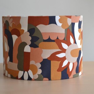 K&ouml;nnte beinhalten: Ein Lampenschirm mit einem farbenfrohen geometrischen Muster in Orange-, Braun-, Gr&uuml;n- und Blaut&ouml;nen. Das Muster zeigt abstrakte Formen und Blumen.