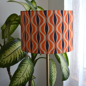 May include: A floor lamp with a drum shade featuring a retro orange, white, and navy blue wavy pattern.
