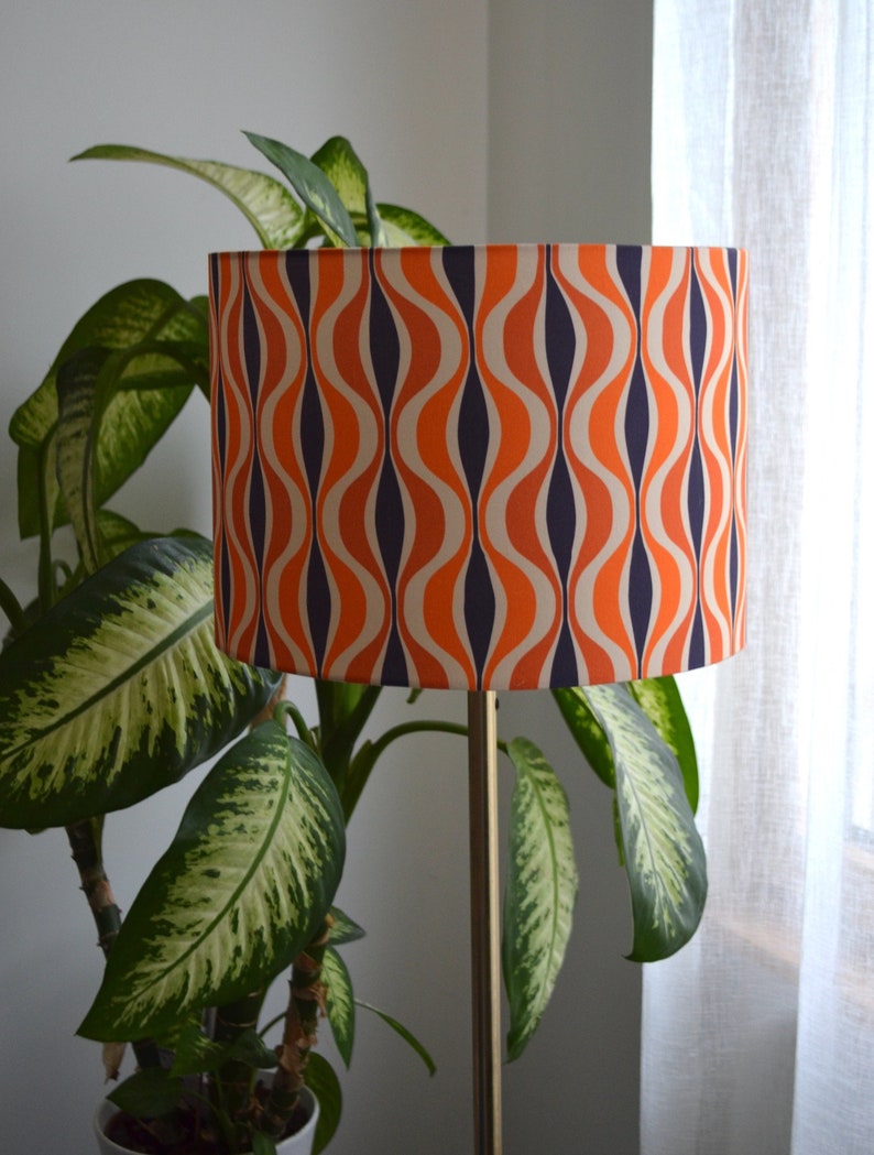 May include: A floor lamp with a drum shade featuring a retro orange, white, and navy blue wavy pattern.