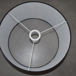 May include: A circular lamp shade featuring a black exterior and a white interior lining. The structure includes a white metal spider fitter with three spokes connecting to a central ring, designed for attachment to a lamp base or fixture.