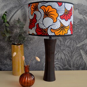 May include: A table lamp with a dark brown wooden base and a cylindrical lampshade featuring a vibrant pattern of orange, red, and yellow fan-shaped motifs against a white background with thin black lines, finished with a black trim.