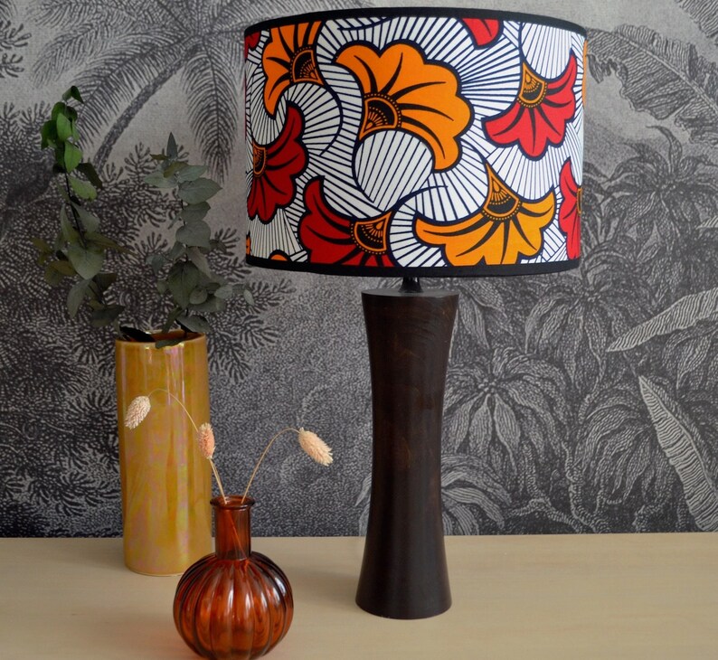 May include: A table lamp with a dark brown wooden base and a cylindrical lampshade featuring a vibrant pattern of orange, red, and yellow fan-shaped motifs against a white background with thin black lines, finished with a black trim.