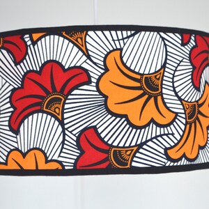 May include: A cylindrical drum lampshade featuring a bold repeating pattern of stylized fan-shaped flowers in vibrant orange and red. The design includes black outlines and fine black radiating lines against a white background with black trim.