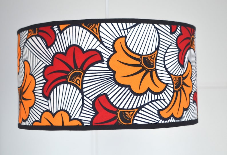 May include: A cylindrical drum lampshade featuring a bold repeating pattern of stylized fan-shaped flowers in vibrant orange and red. The design includes black outlines and fine black radiating lines against a white background with black trim.