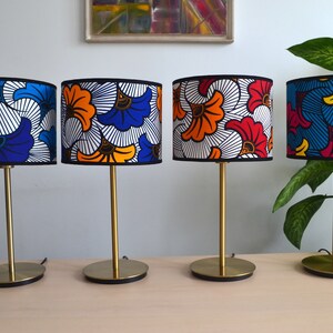 May include: Four table lamps with cylindrical fabric shades featuring vibrant, multi-colored floral patterns in blue, orange, red, yellow, and white. Each lamp has a slender gold-toned metal stem and a circular gold-toned base with black trim.