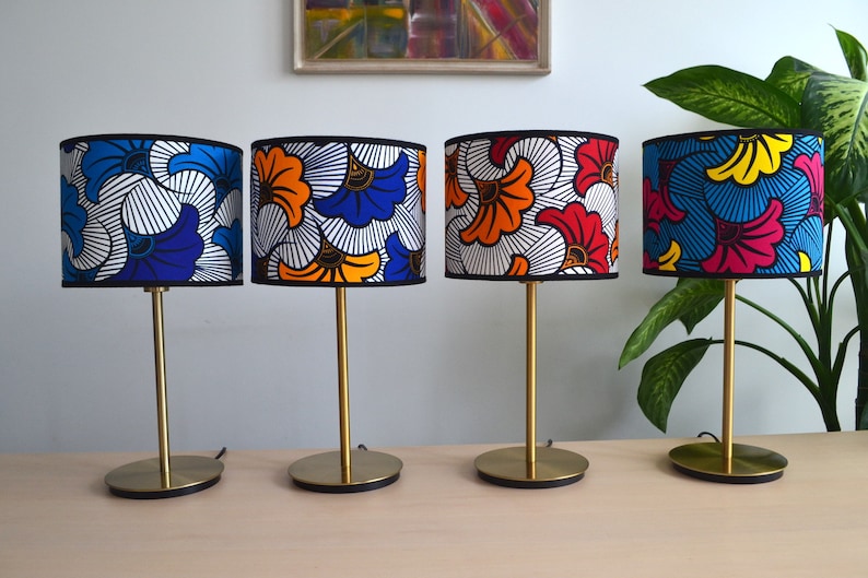 May include: Four table lamps with cylindrical fabric shades featuring vibrant, multi-colored floral patterns in blue, orange, red, yellow, and white. Each lamp has a slender gold-toned metal stem and a circular gold-toned base with black trim.