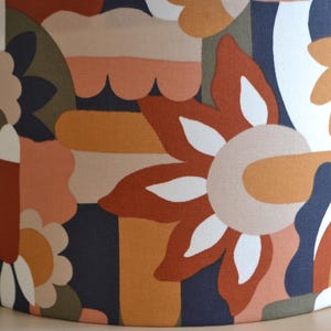 K&ouml;nnte beinhalten: Ein Lampenschirm mit einem farbenfrohen geometrischen Muster mit abstrakten Formen, Blumen und Wirbeln in Orange-, Braun-, Wei&szlig;- und Blaut&ouml;nen.
