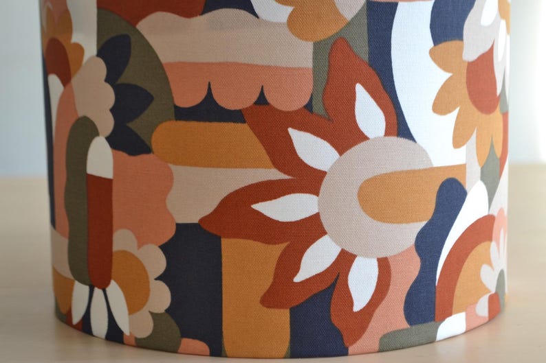 K&ouml;nnte beinhalten: Ein Lampenschirm mit einem farbenfrohen geometrischen Muster mit abstrakten Formen, Blumen und Wirbeln in Orange-, Braun-, Wei&szlig;- und Blaut&ouml;nen.