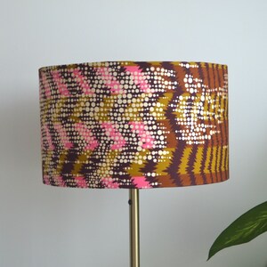 May include: A brown, pink, and gold lampshade with a geometric pattern. The lampshade is made of fabric and has a cylindrical shape.