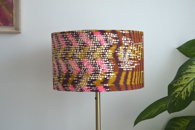 May include: A brown, pink, and gold lampshade with a geometric pattern. The lampshade is made of fabric and has a cylindrical shape.