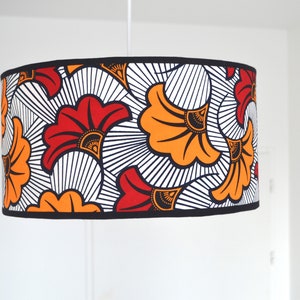 May include: A cylindrical drum lampshade featuring a bold graphic pattern of stylized red and orange fan-shaped flowers against a white background with black line details. The top and bottom edges are finished with a solid black fabric trim.