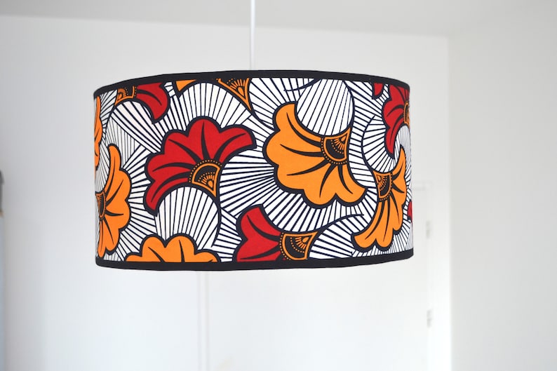 May include: A cylindrical drum lampshade featuring a bold graphic pattern of stylized red and orange fan-shaped flowers against a white background with black line details. The top and bottom edges are finished with a solid black fabric trim.