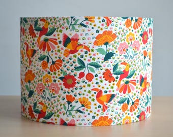 May include: A white lampshade with a colorful floral and bird print. The print features toucans, flowers, and leaves in shades of orange, red, green, and yellow.