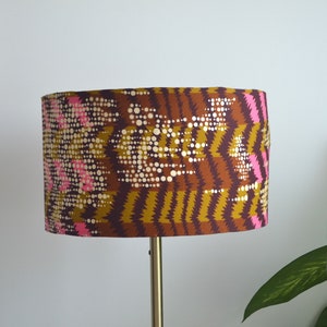 May include: A brown and gold lampshade with a pink and white geometric pattern. The lampshade is cylindrical and has a smooth surface.