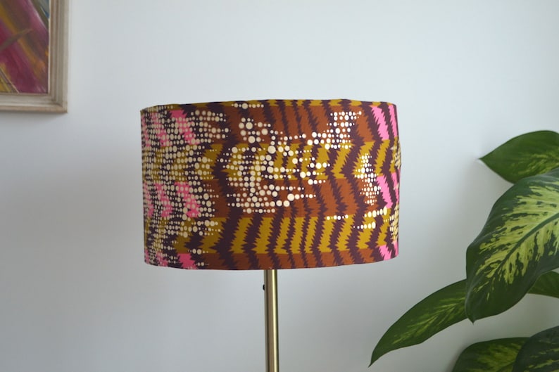 May include: A brown and gold lampshade with a pink and white geometric pattern. The lampshade is cylindrical and has a smooth surface.