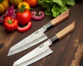 May include: Two Jayger brand kitchen knives with wooden handles. The larger knife has a Damascus steel blade and the smaller knife has a plain steel blade. Both knives are on a wooden cutting board with vegetables in the background.