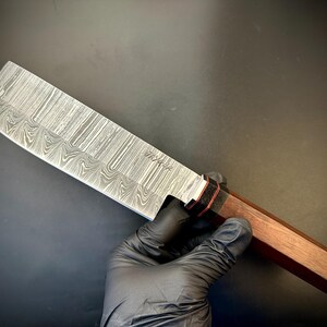 May include: A Damascus steel chef's knife with a wooden handle. The blade has a wavy pattern and the handle is a dark brown color.