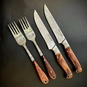 Può includere: Set di quattro utensili da cucina con manici in legno. Due forchette e due coltelli con finitura in acciaio damascato. I coltelli sono etichettati "Waygee".