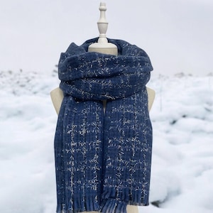 May include: A blue scarf with silver thread woven throughout. The scarf is displayed on a white mannequin against a snowy background.