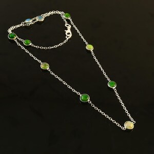 May include: A silver necklace featuring a delicate chain design. The necklace is adorned with several round, vibrant green gemstones. The gemstones are evenly spaced along the chain, creating a simple yet elegant look. The necklace is displayed against a black background.