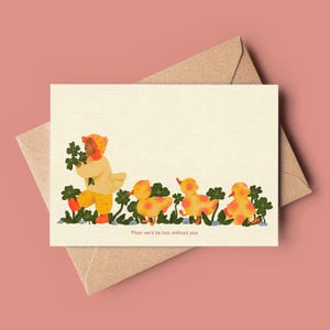 Op de afbeelding: Wenskaart met een illustratie van een kind in gele kleding met klavers, gevolgd door drie eendjes. De tekst "Mom we'd be lost without you" staat onderaan. De kaart ligt op een roze achtergrond en een bruine envelop.